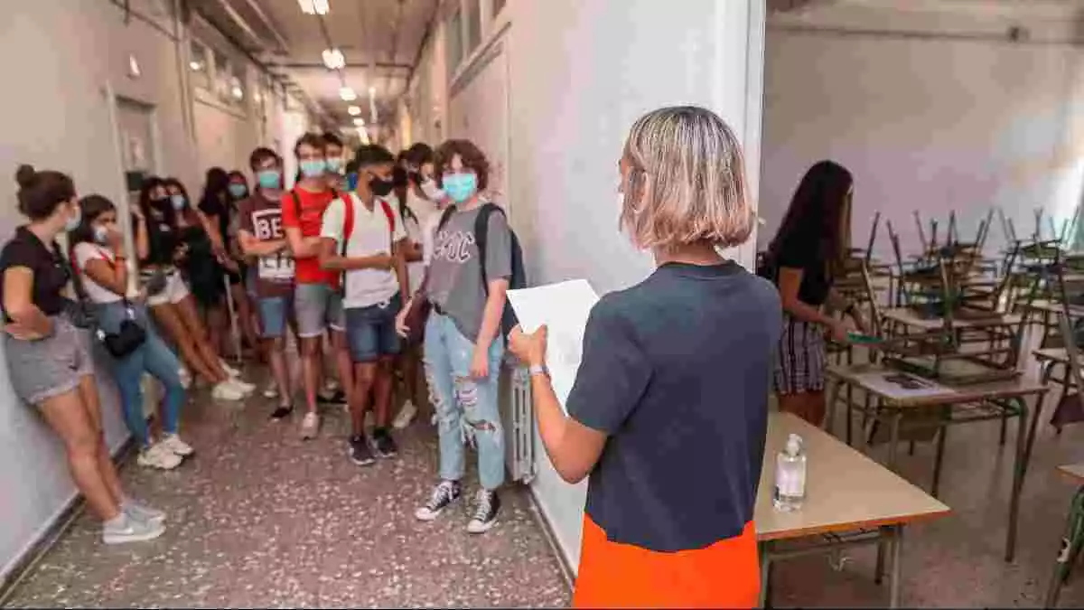 Imatge de diversos alumnes i una porfessora amb mascaretes esperant a entrar a una aula