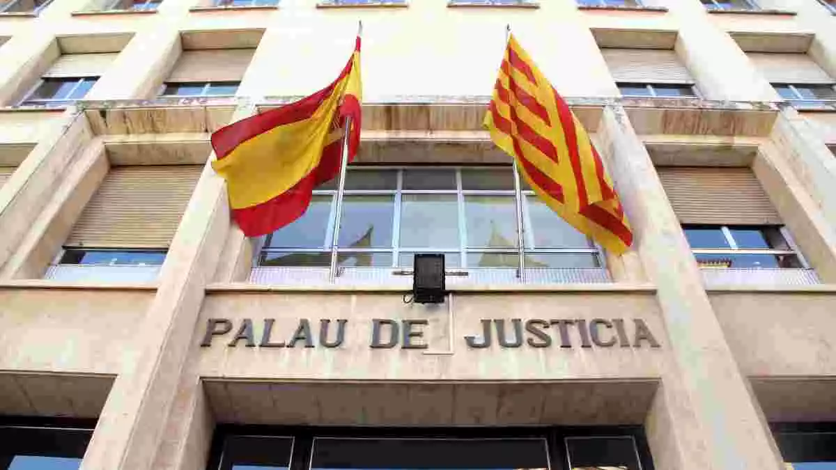 Pla contrapicat de la façana d'entrada a l'Audiència de Tarragona, amb el rètol de 'Palau de Justícia' i les banderes espanyola i catalana.