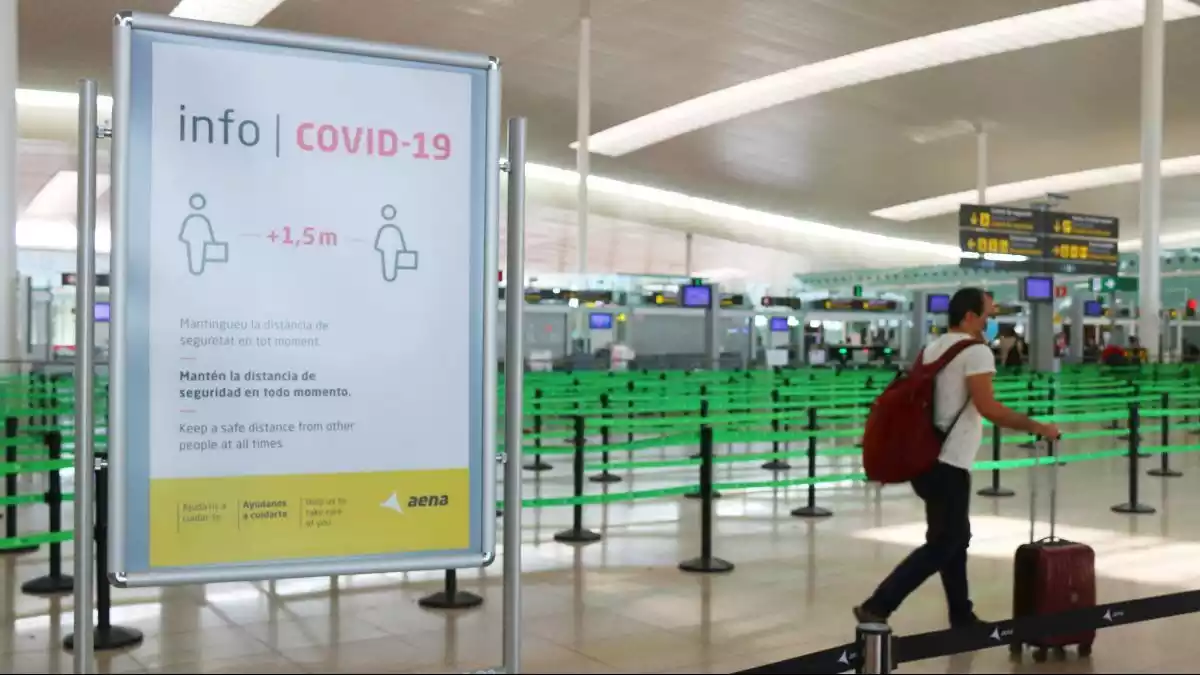 Pla general d'un cartell informatiu de la Covid-19 i un passatger a la T1 de l'Aeroport del Prat, pràcticament buit.