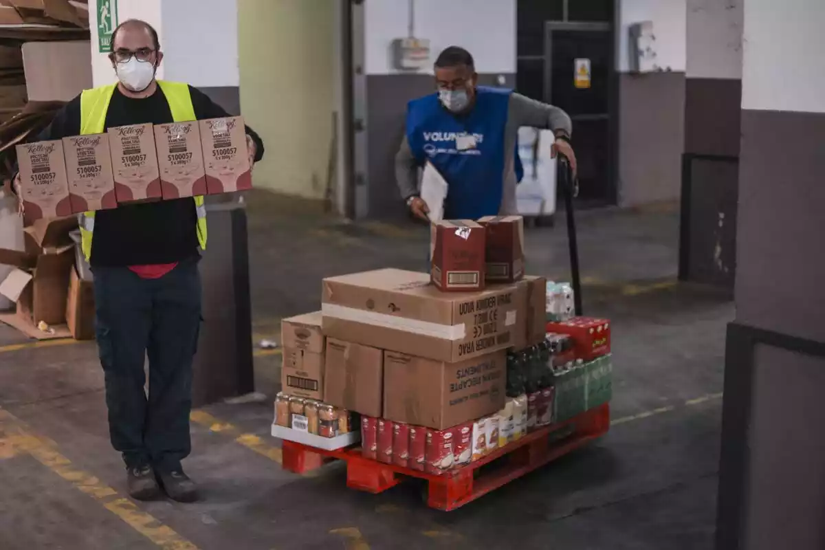 Dos voluntaris del Banc dels Aliments transportant un palet amb menjar