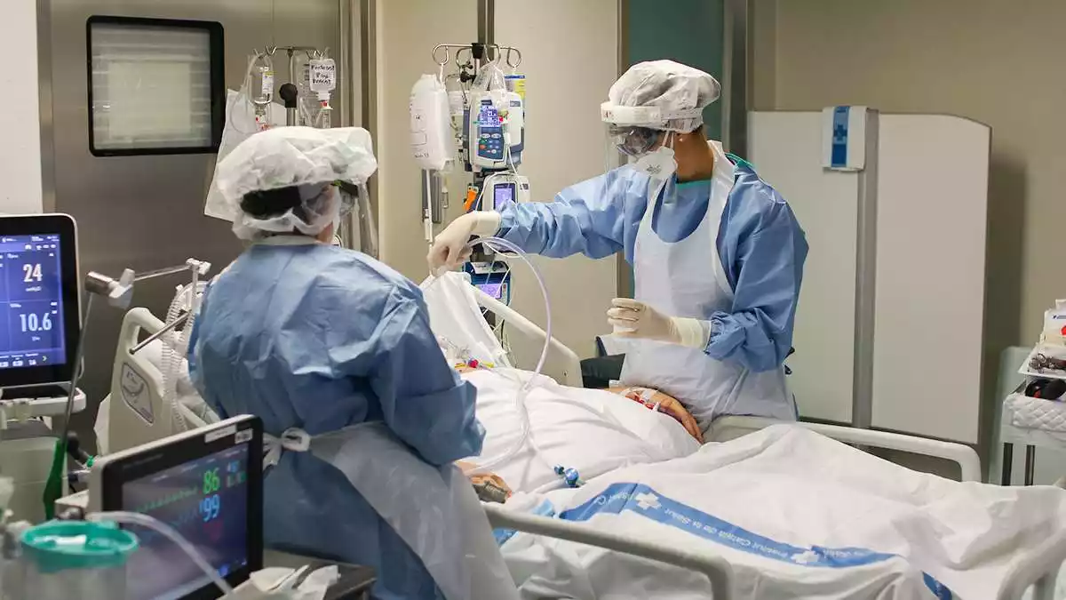 Pla mitjà de dues infermeres atenent una pacient de Covid-19 ingressada al servei de Medicina Intensiva de l'Hospital Verge de la Cinta