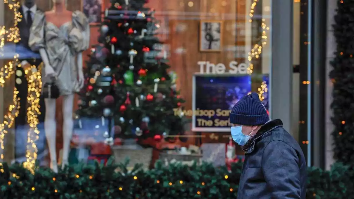 Un home amb mascareta passant per davant d'un arbre de Nadal i decoració diversa