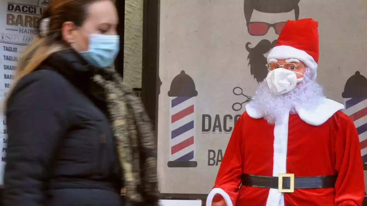 Una dona amb mascareta passant al costat d'un Papà Noel amb mascareta