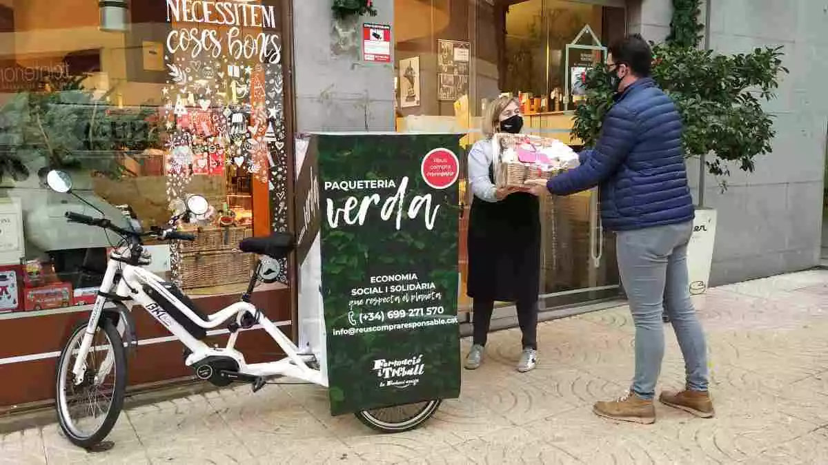 Una persona lliura un paquet a un treballador de Reus Compra Responsable davant de l'establiment, amb la bicicleta de repartiment al costat