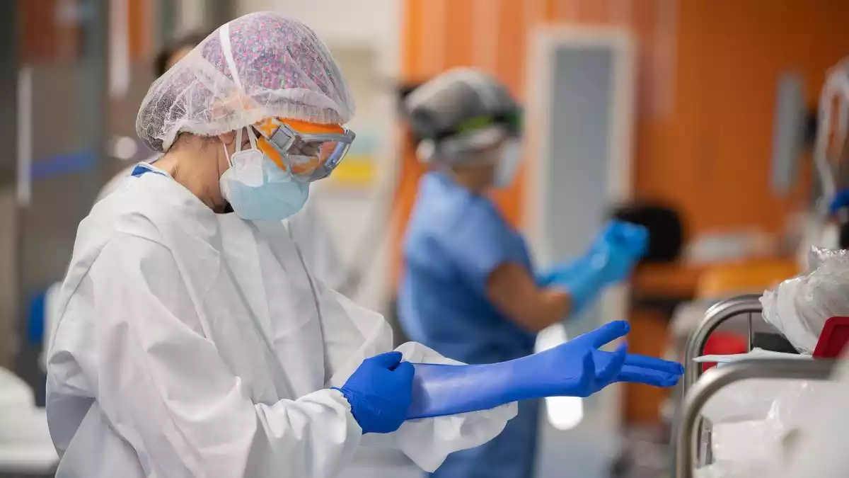 Pla mitjà d'una professional sanitària del Clínic posant-se guants de protecció a l'UCI amb malalts de covid