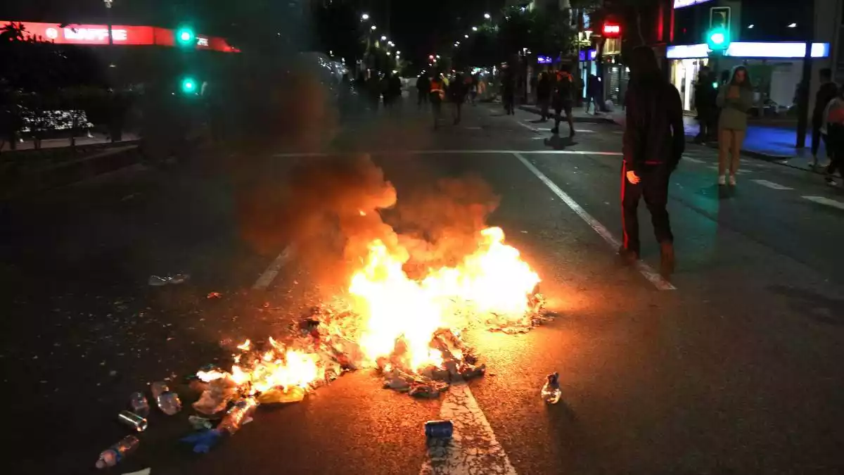 Pla general de brossa cremant al terra i d'un manifestant al carrer Prat de la Riba de Tarragona a l'inici dels aldarulls el 17 d'octubre del 2019