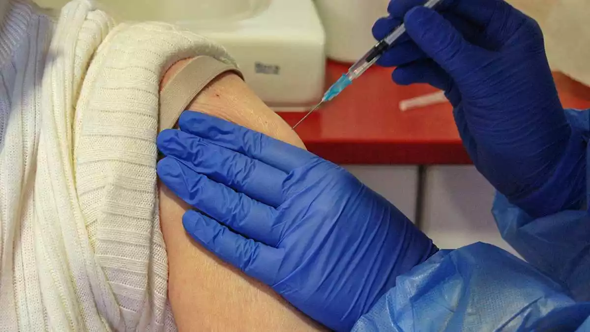 Pla tancat de l'agulla d'una xeringa amb la segona dosi de la vacuna contra la covid-19 a punt de punxar el braç d'una dona