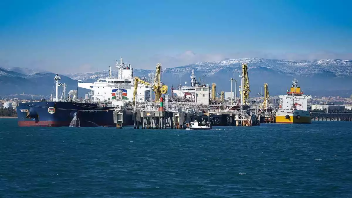 Imatge de diversos vaixells atracats al pantalà de Repsol al port de Tarragona, amb muntanyes enfarinades al fons
