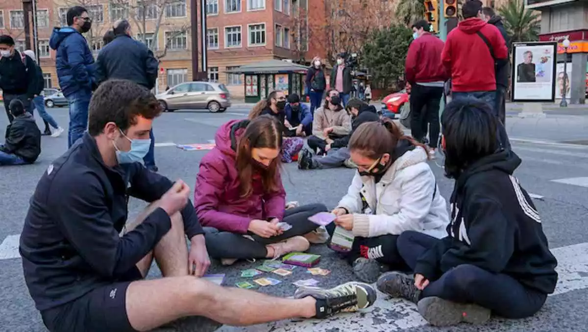 Manifestants asseguts a terra i jugant a cartes en el tall de la Imperial Tàrraco a Tarragona per demanar la llibertat de Pablo Hasel i Cristian Mestre
