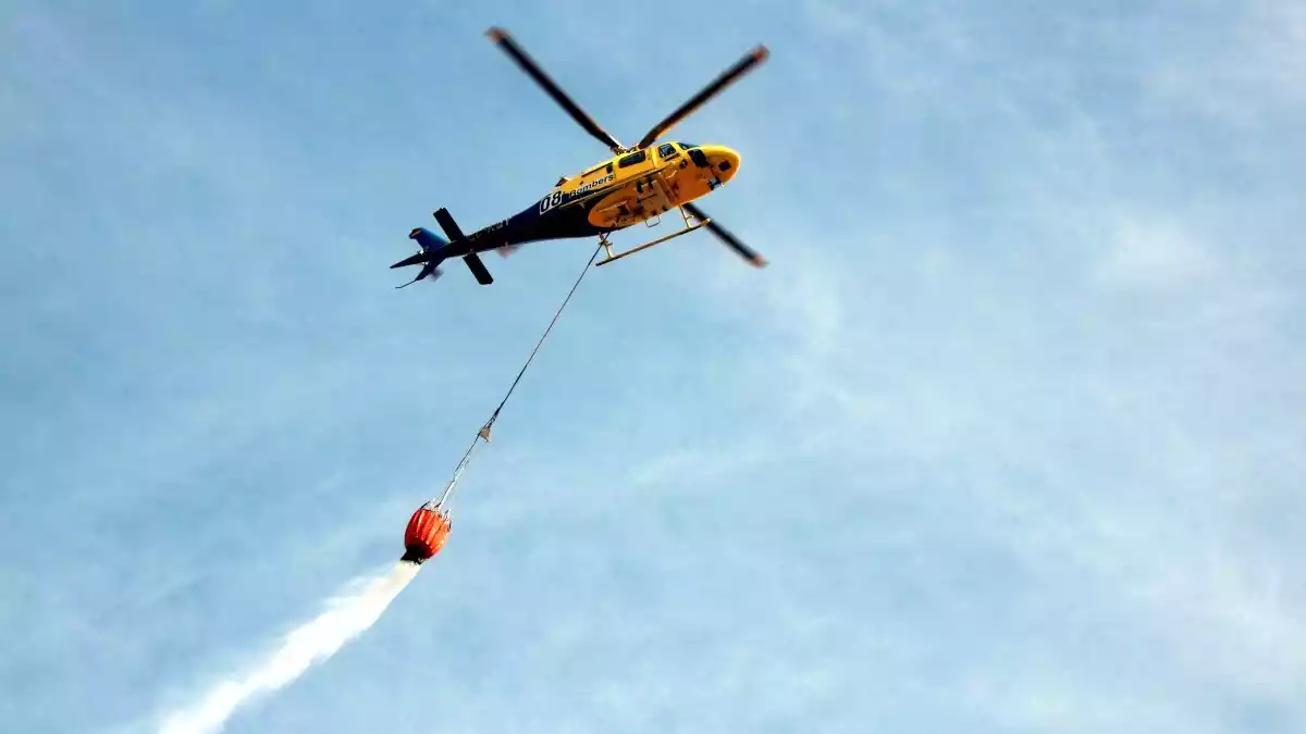 Pla general d'un helicòpter buidant una càrrega d'aigua en una zona afectada per un incendi