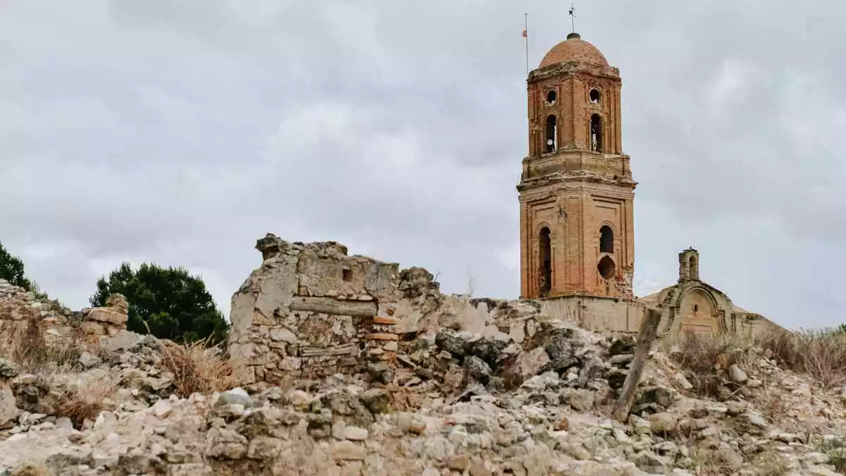 Imatge del campanar de l'església del Poble Vell de Corbera d'Ebre, amb un edifici en ruïnes al davant