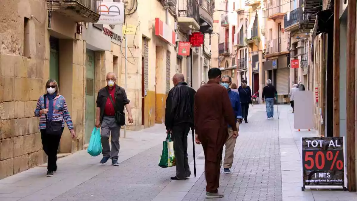 Pla general del carrer de Sant Blai, un dels principals eixos comercials de Tortosa, amb diverses persones passejant.