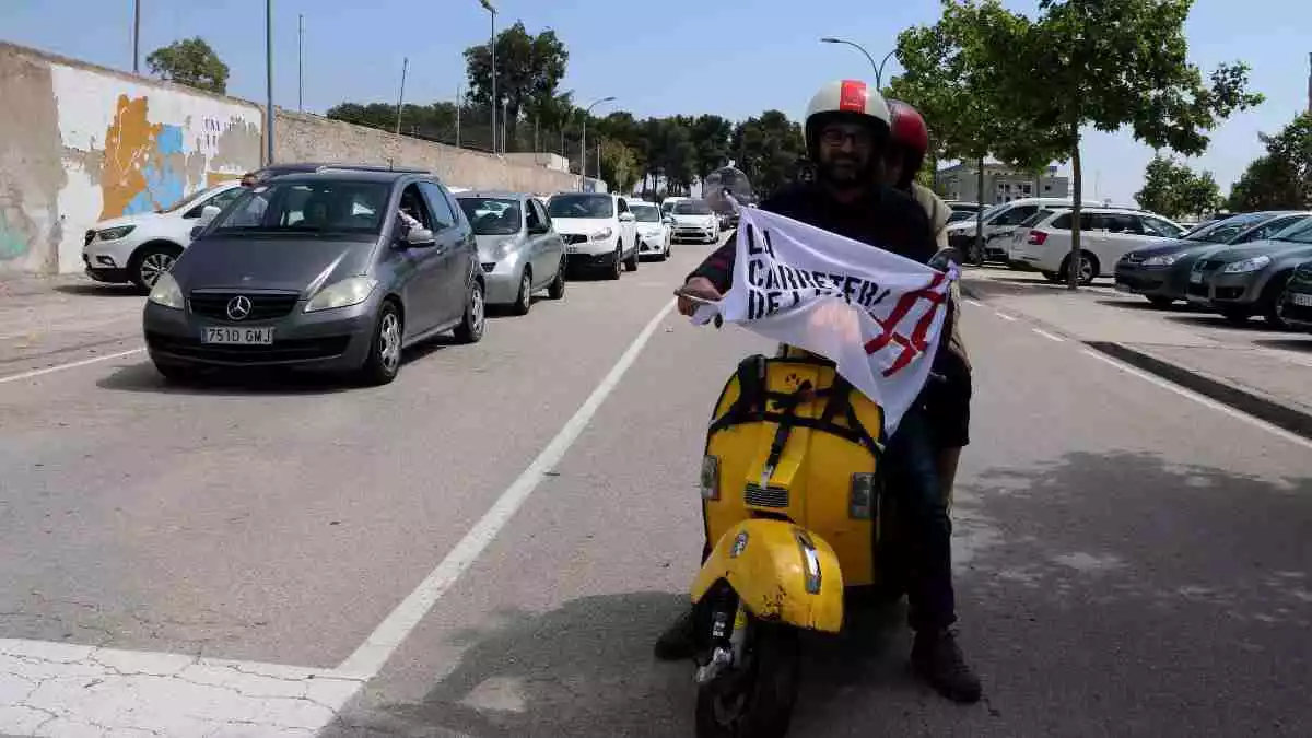 Imatge dels vehicles i una moto amb un cartell reivindicatiu al començament de la marxa lenta