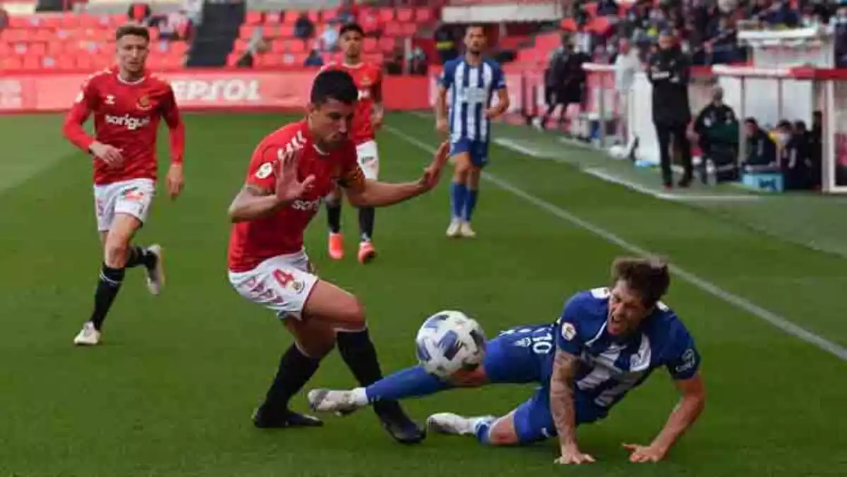 Un jugador de futbol cau a terra per la pressió d'un altre