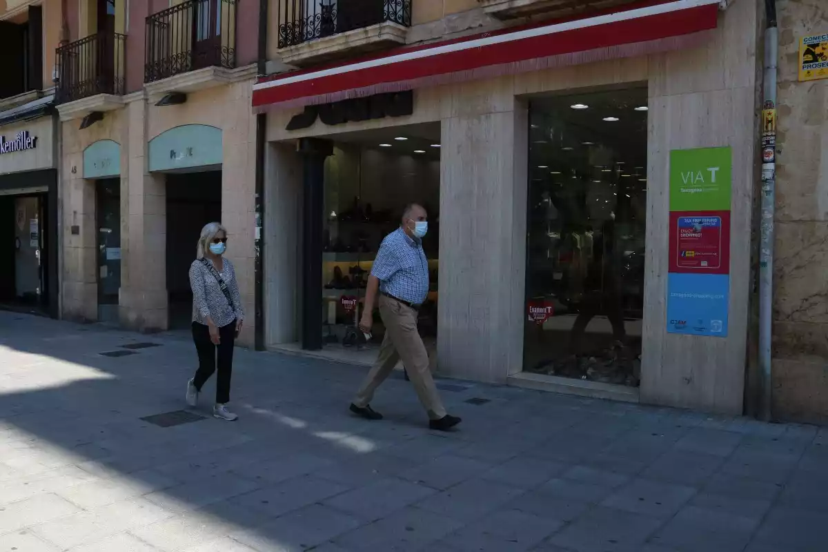 Pla general de dos vianants amb mascareta davant d'establiments comercials a la Rambla Nova de Tarragona
