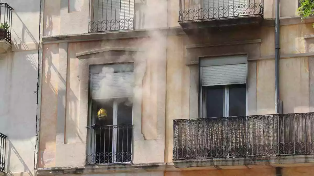 Pla obert del balcó del pis de la Rambla Nova, 10, on s'ha originat el foc, amb un bomber obrint la finestra perquè marxi el fum