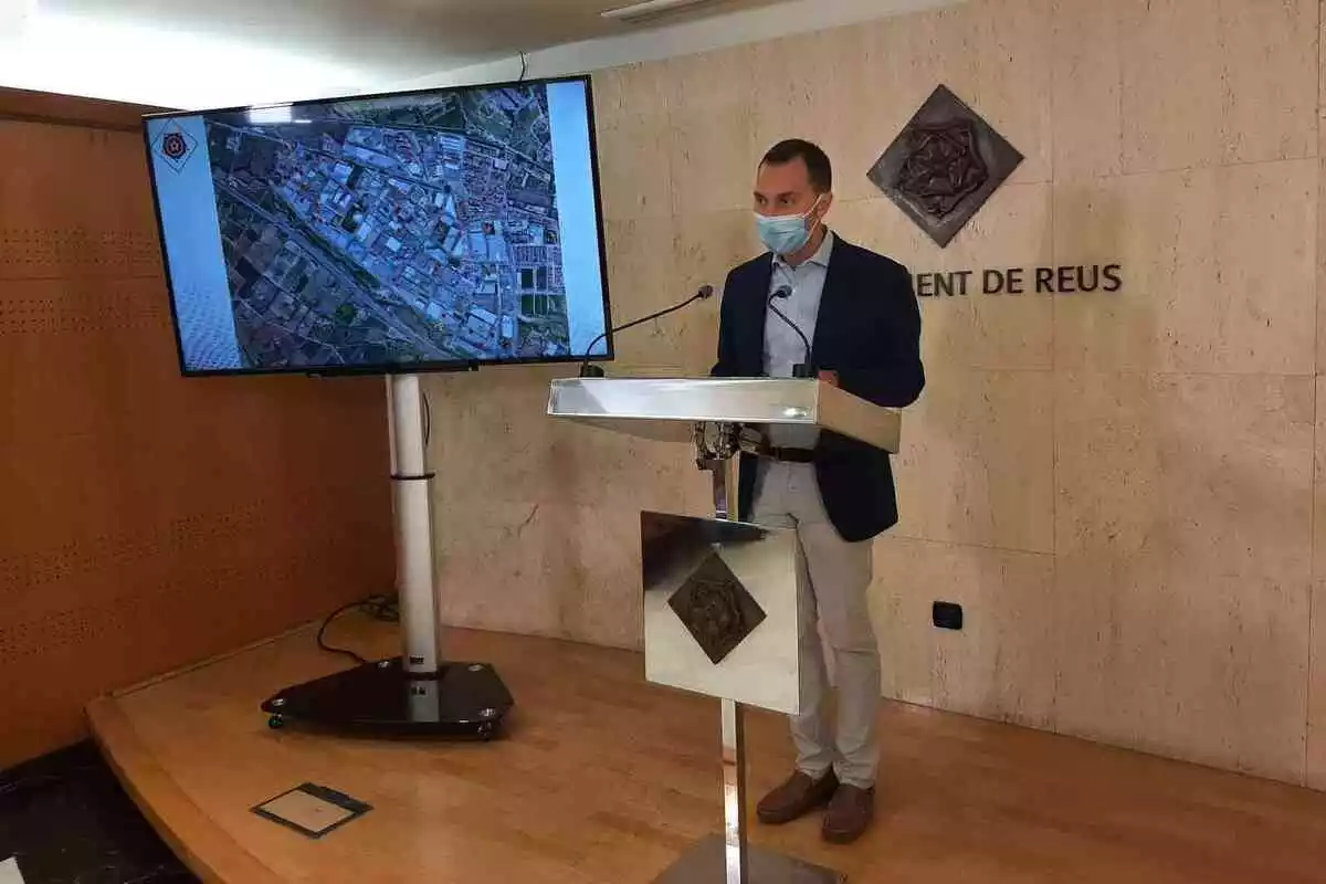 Daniel Rubio al faristol de la sala de premsa de l'Ajuntament de Reus amb una pantalla al costat