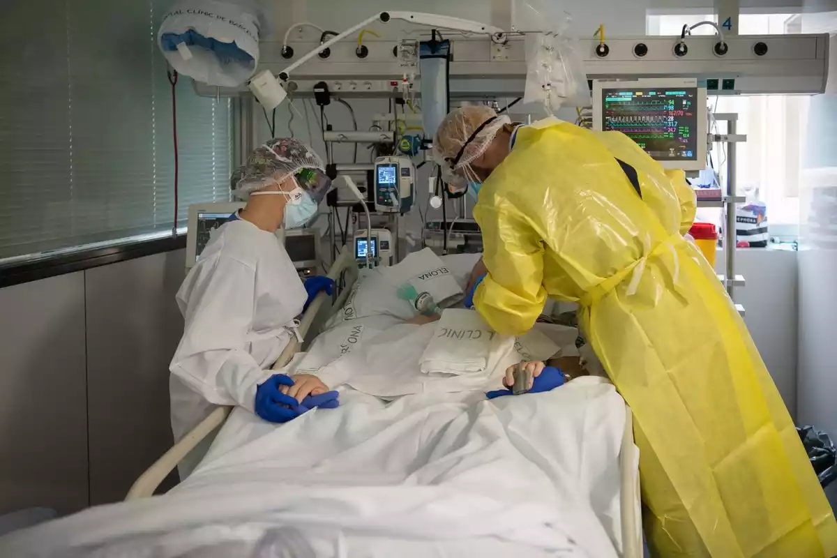 Pla mitjà de dos sanitaris visitant un pacient de covid a l'UCI de l'Hospital Clínic protegits amb EPI