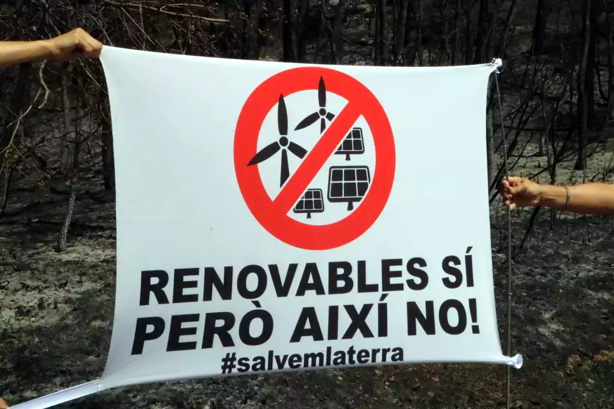 Una pancarta en contra dels macroprojectes solars i eòlics. Al fons, el bosc cremat