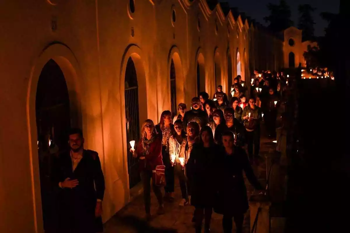 El públic de les visites nocturnes al Cementiri General de Reus amb espelmes seguint un dels personatges protagonistes