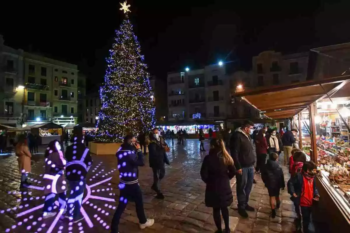 El Mercat de Nadal de Reus del 2020, amb l'arbre al mig, projecció de llums i les parades formant un cercle al voltant de la coca central de la plaça