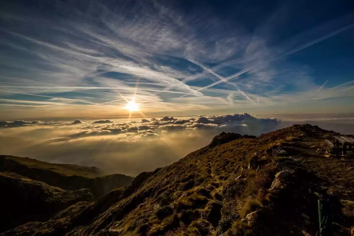 Imatge d'una muntanya amb sol i núvols de fons