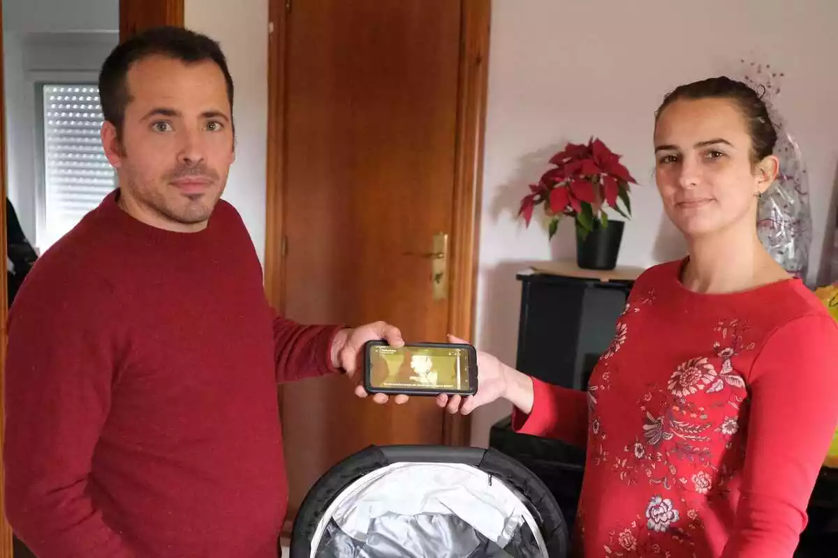 Joaquim i Cristina, a casa seva, amb un cotxet de nadó al mig ensenyen una imatge de l'ecografia que els han enviat per mòbil