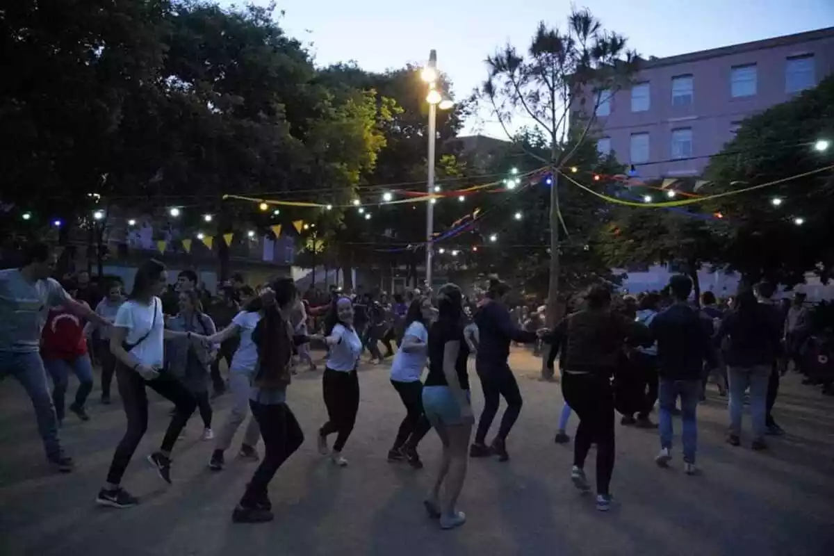 Gent ballant al voltant d'un pi plantat al mig de la plaça de la Patacada de Reus