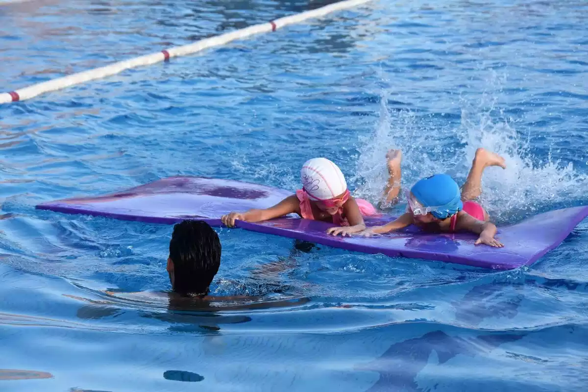 Imatge de dues nenes sobre una taula aprenent a nedar