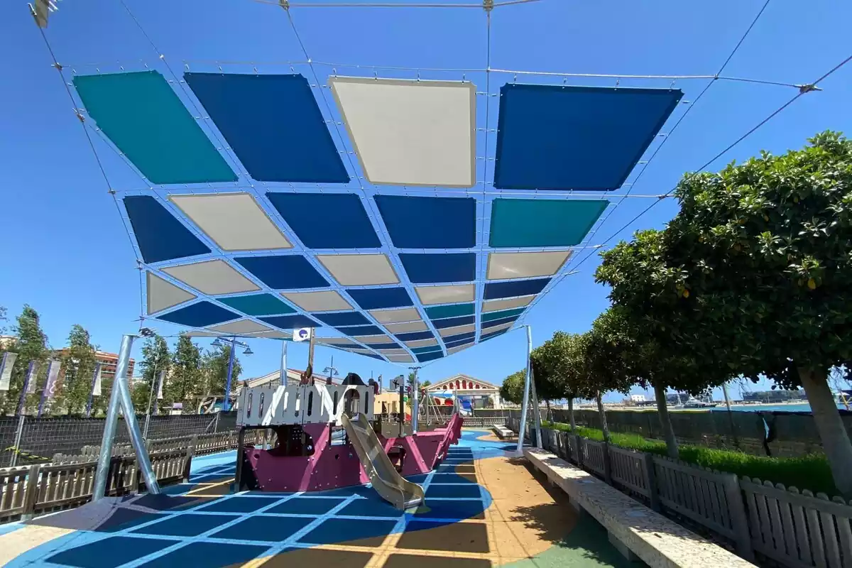 Imatge d'un dels parcs infantils del Moll de Costa amb el tendal que projecta ombra sobre el mobiliari