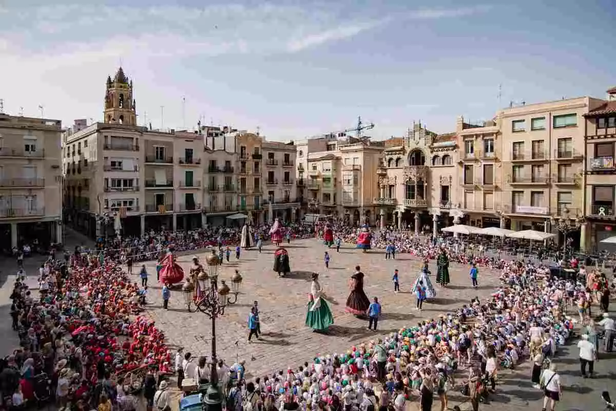 La plaça del Mercadal de Reus amb els Gegants ballant al centre i centenars d'infants asseguts al voltant mirant-los