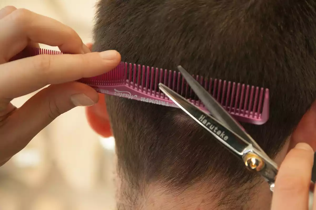 Un perruquer tallant el cabell d'un jove