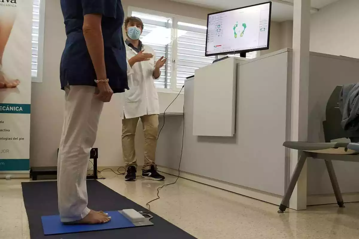 Un podòleg parla amb una pacient, que té el peu en una estora que escaneja connectada a una pantalla d'ordinador