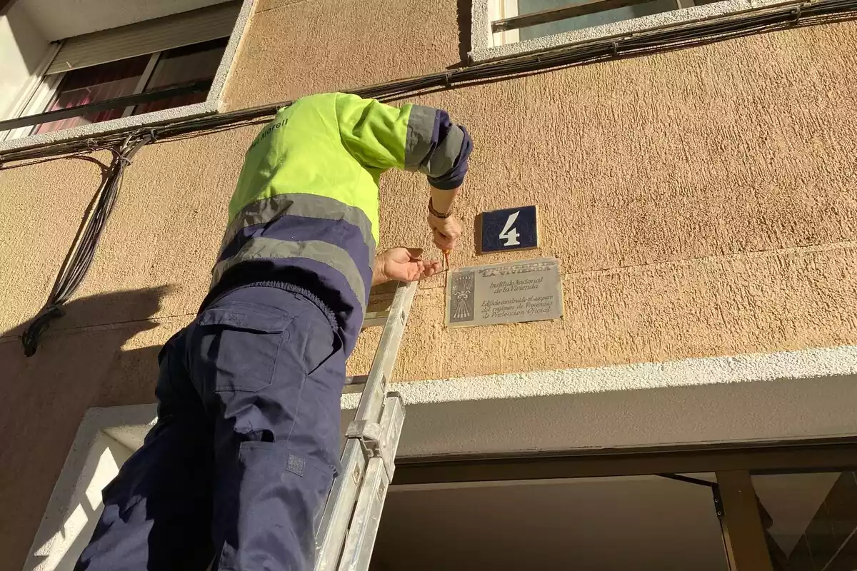Imatge d'un treballador municipal retirant una placa franquista de la façana d'un edifici