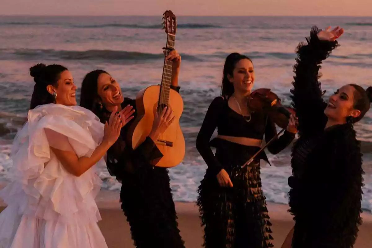 Las Migas en una imatge promocional a la platja, tocant una guitarra, un violí i picant de mans