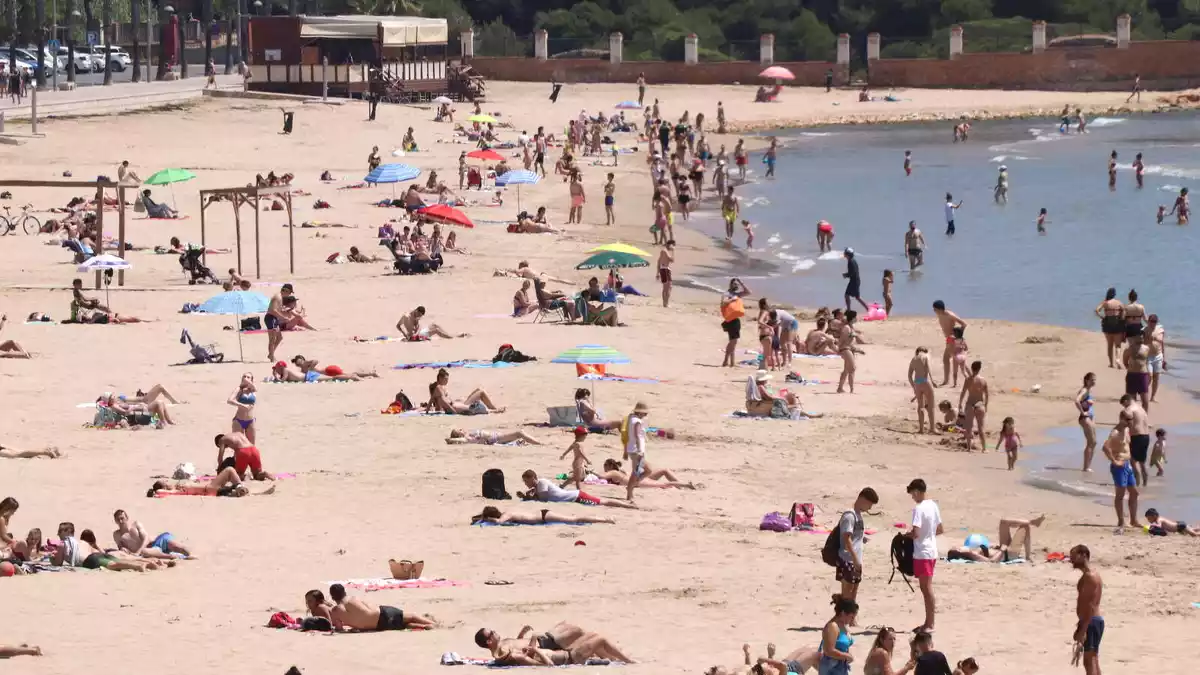 Pla mitjà de la platja de l'Arrabassada de Tarragona, amb banyistes i gent prenent el sol.
