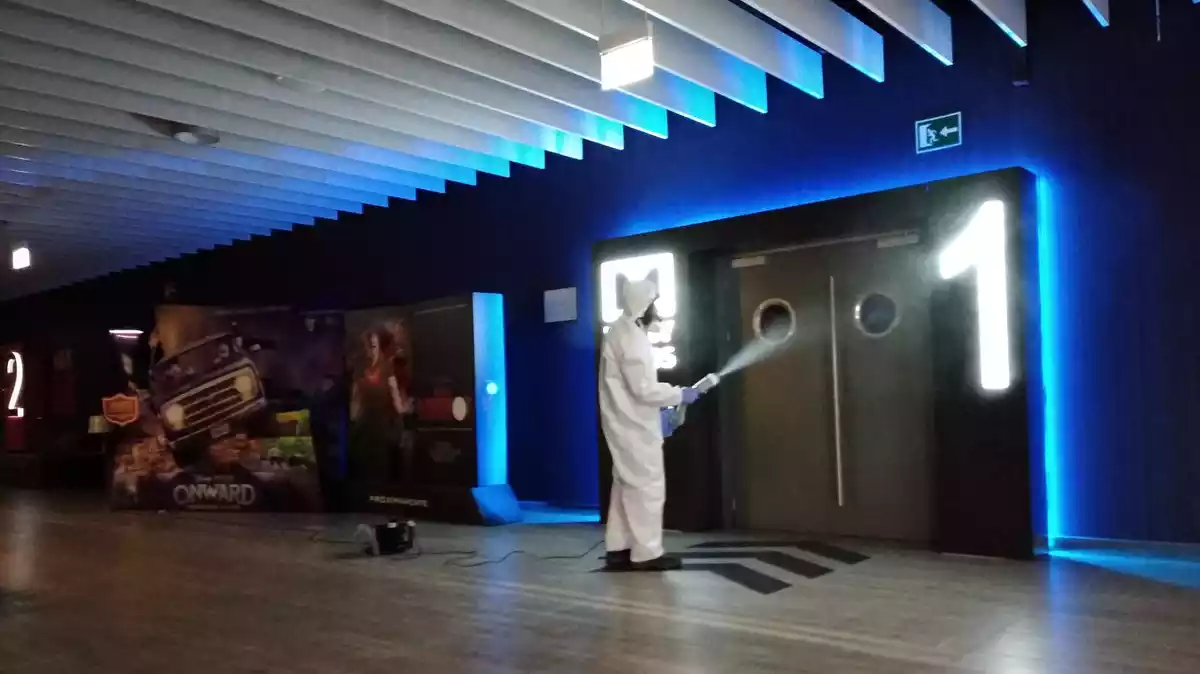 Imatge d'un treballador desinfectant l'accés d'una sala de cinema