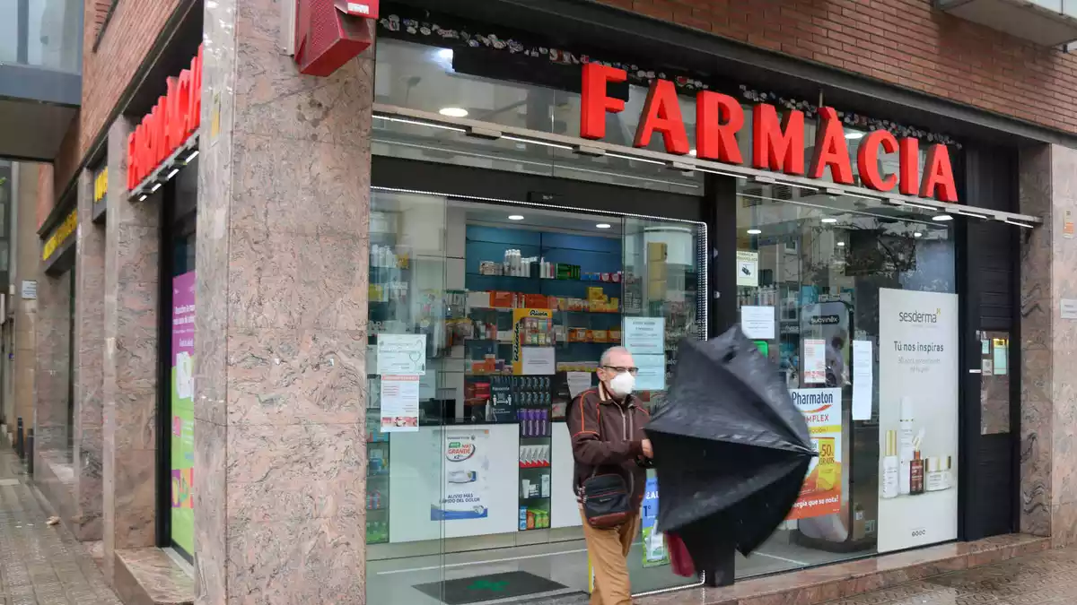 Un home obre un paraigües a la sortida d'una farmàcia el 20 d'abril del 2020