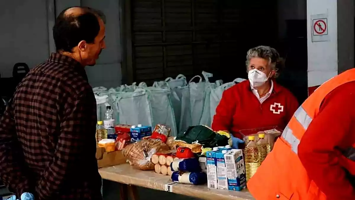 Una voluntària de Creu Roja darrere d'una taula plena d'aliments