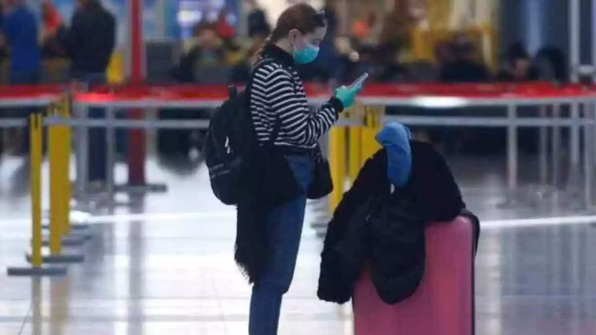Una turista con mascarilla y guantes en un aeropuerto.