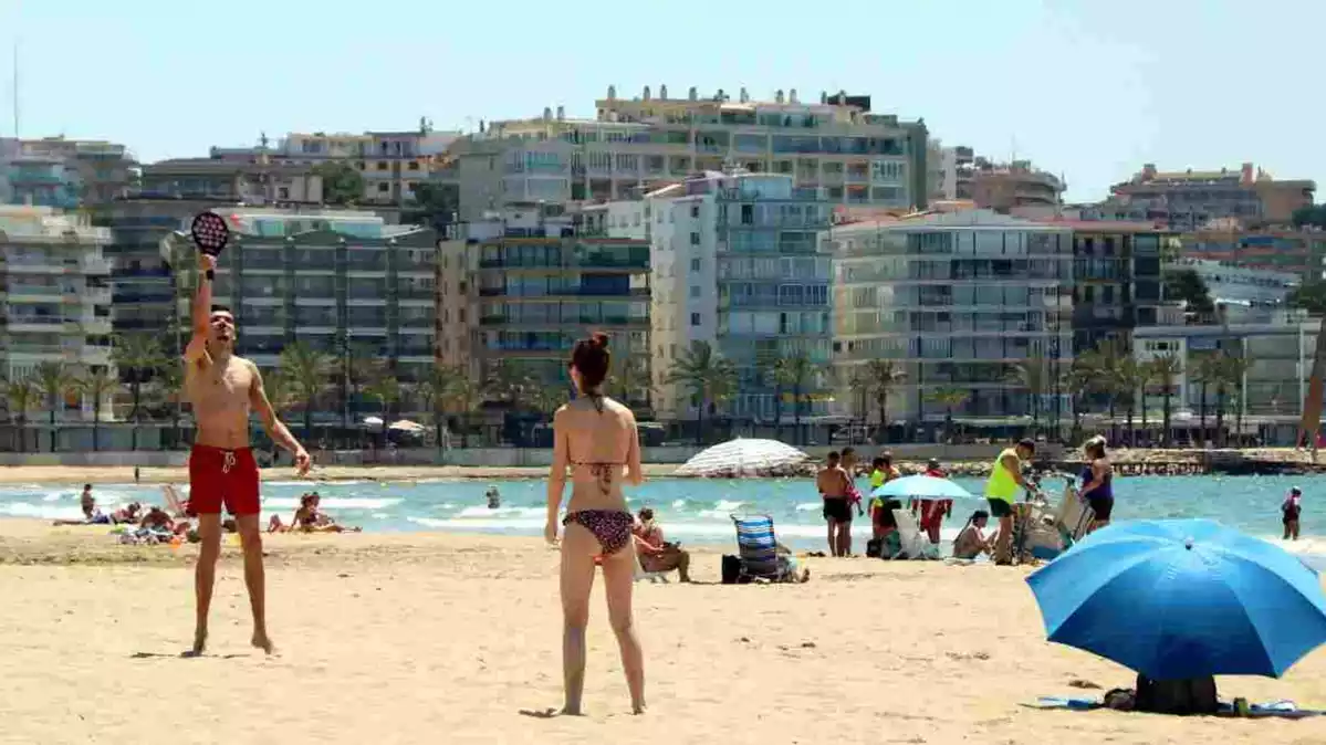 Pla sencer d'un noi i una noia jugant a les pales a la platja de Salou, amb diverses persones prenent el sol el 29 de maig del 2020.