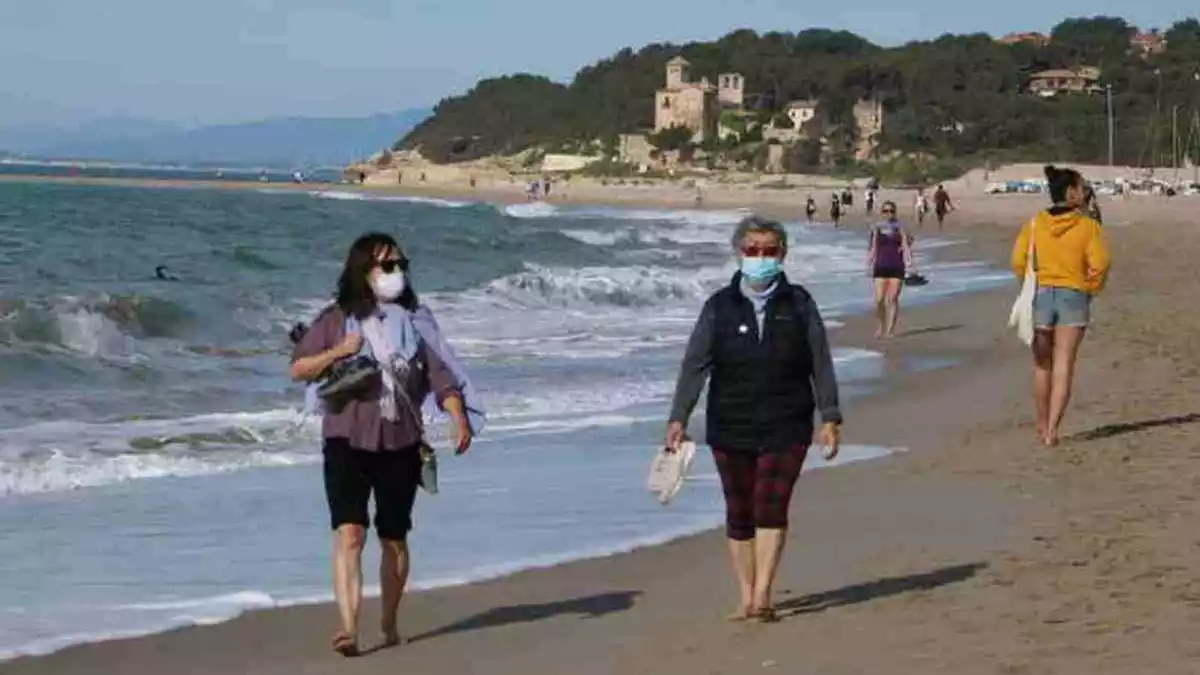 Pla general de dues dones amb mascareta caminant per la platja d'Altafulla en el primer dia permès per sortir a practicar esport