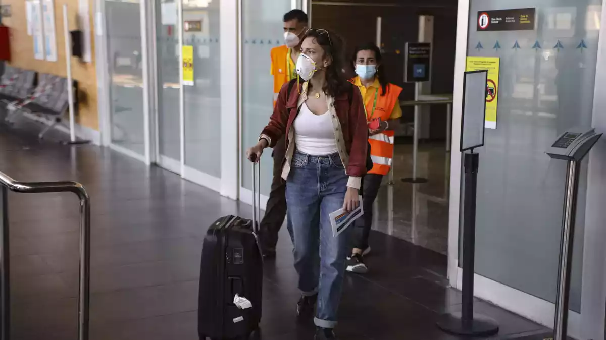 Una passatgera arriba a l'Aeroport de Reus, amb una maleta en una mà, un formulari a l'altra i la mascareta posada