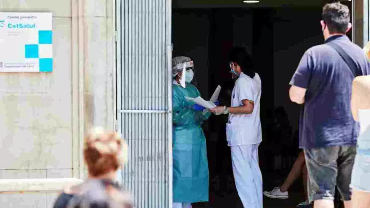 Sanitaris a les portes d'un hospital, amb mascaretes i equips protectors, mentre els pacients fan cua fora de l'edifici