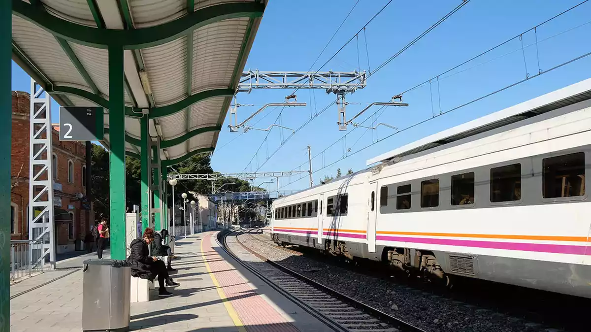 Un tren aturat a l'estació de Vila-seca mentre diversos viatgers s'esperen a l'andana.