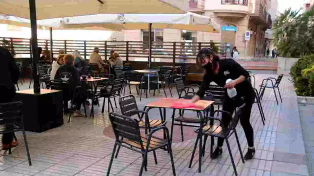 Una cambrera netejant una taula buida a la terrassa d'un local a Tortosa