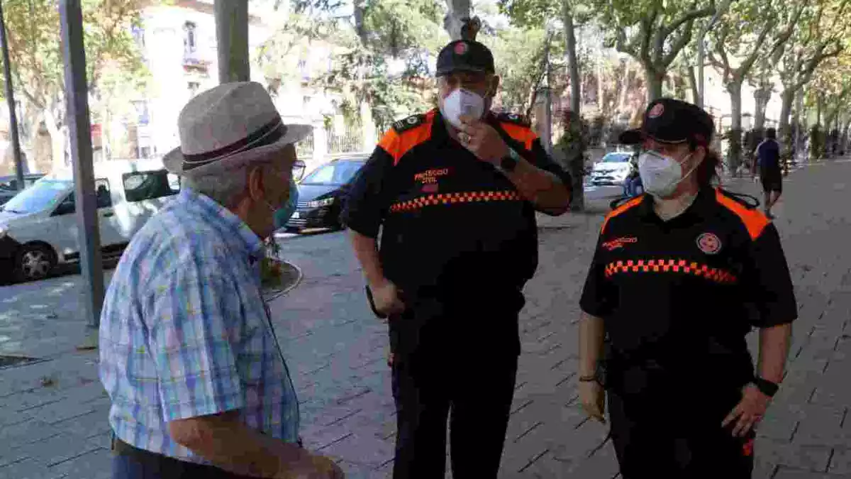 Dos agents de Protecció Civil amb mascareta aconsellant un home gran a Reus