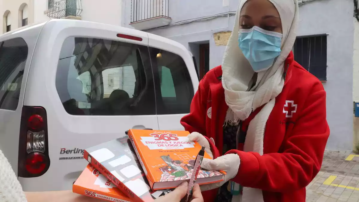 Pla mitjà d'una tècnica de Creu Roja Joventut a Tarragona, entregant llibres a la mare d'un infant, el dia de Sant Jordi.