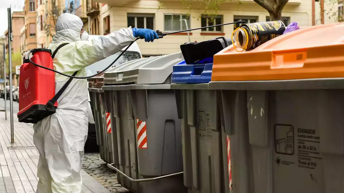 Un operari del servei de neteja viària de Reus desinfecta una illa de contenidors, alguns dels quals són plens