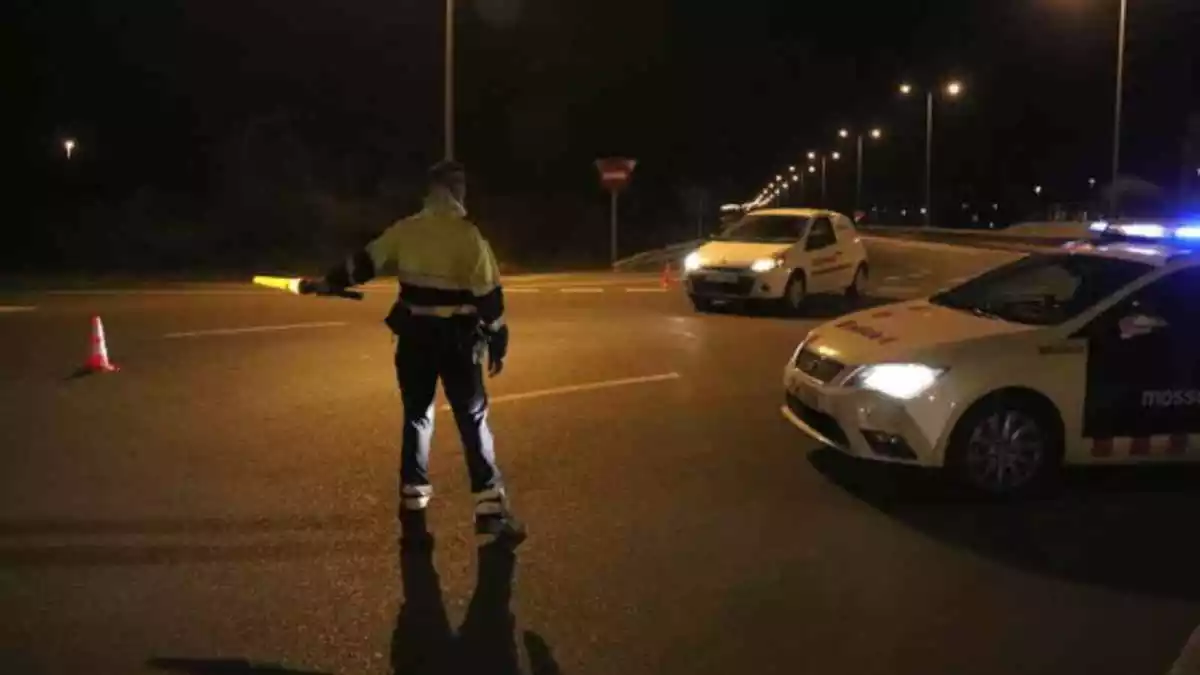 Un mosso d'esquadra de nit amb el cotxe policial al costat i un vehicle blanc apropant-se